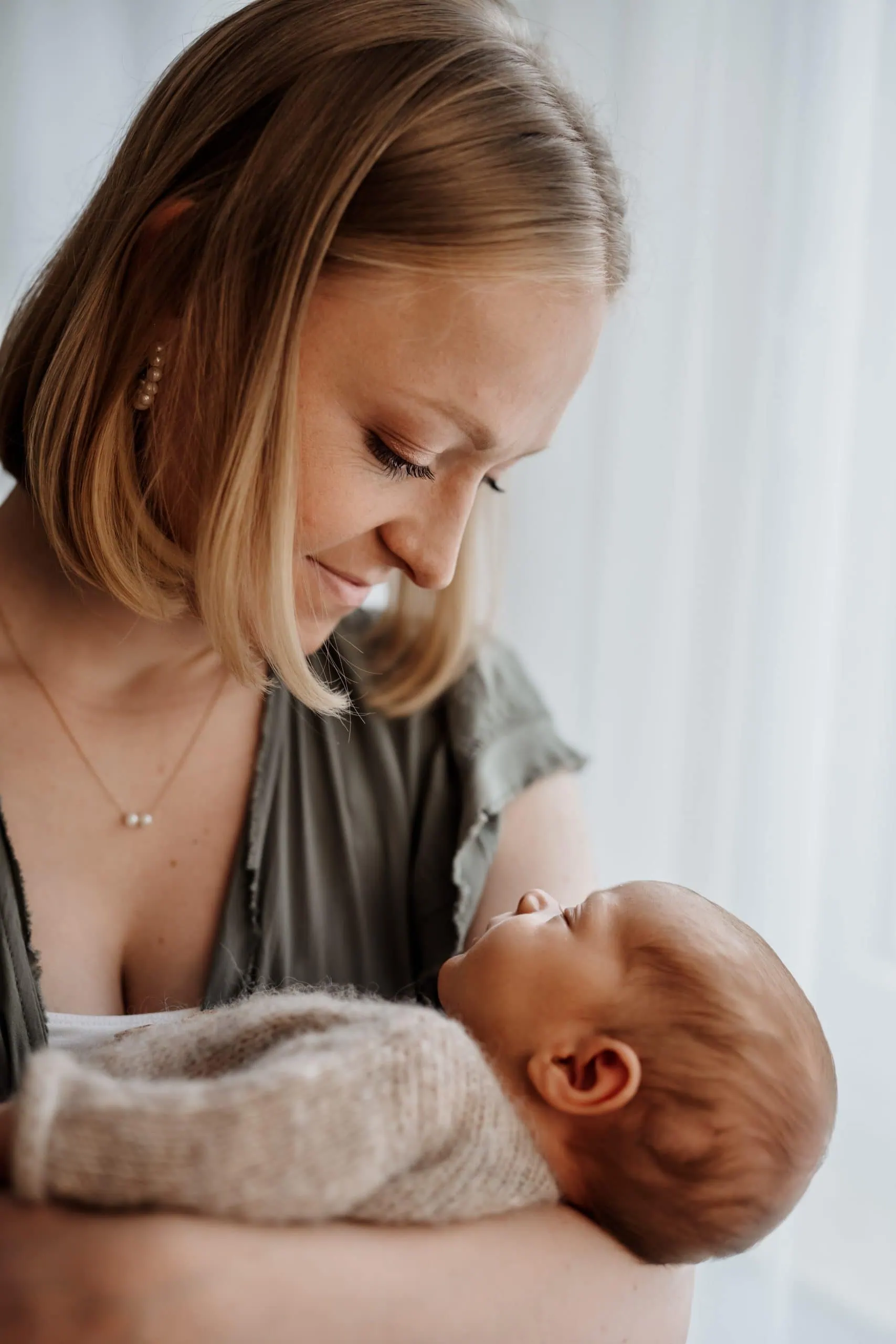 Baby auf Mamas Arm Mama hält ihr Neugeborenes ganz sanft und trägt Kleider aus dem Kundenkleiderschrank von Monja Drössel