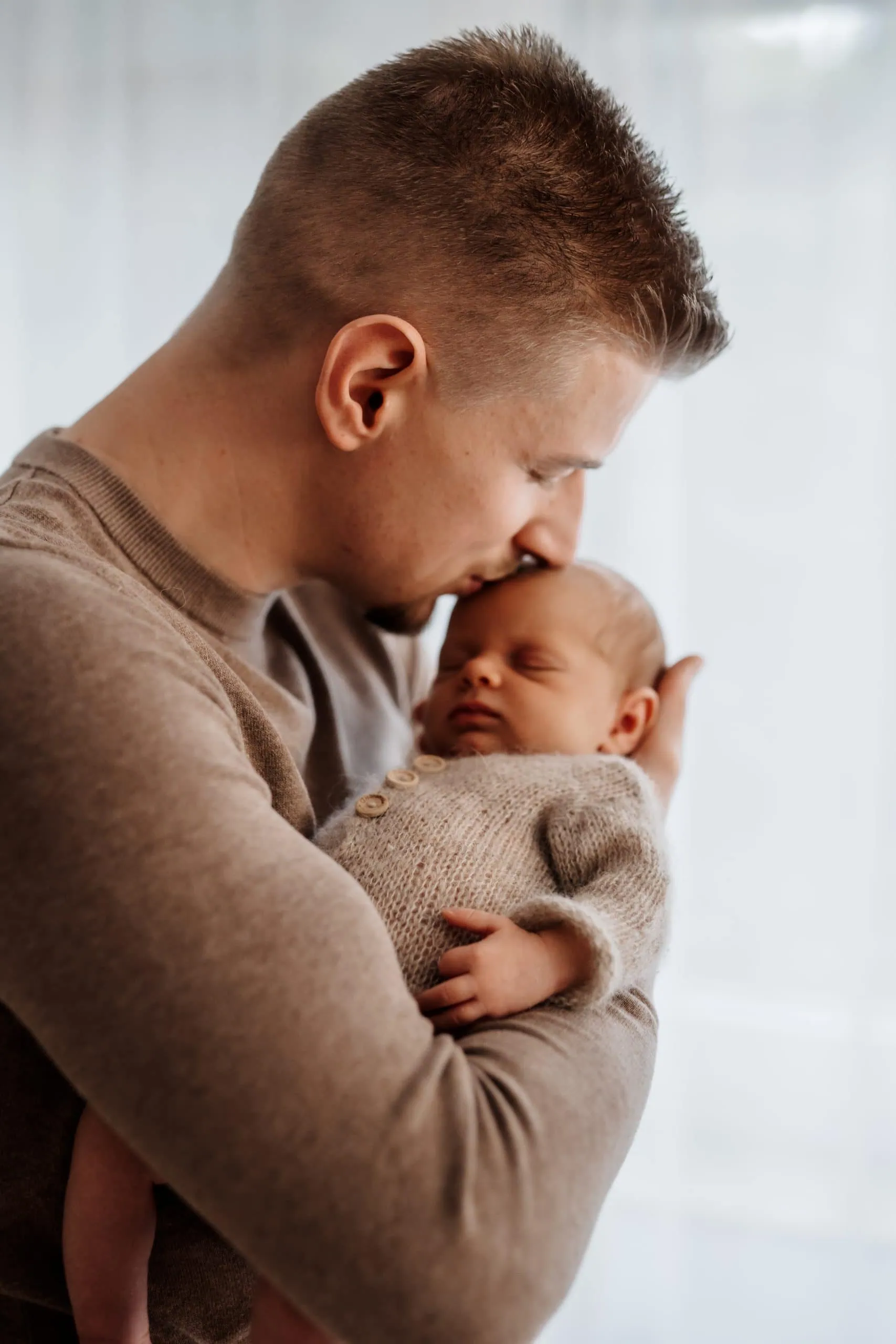 Papa küsst neugeborenes Baby sanft und hält es im Arm Familienfotografin Monja Drössel fotografiert Neugeborenes in der Nähe von Villingen Schwenningen